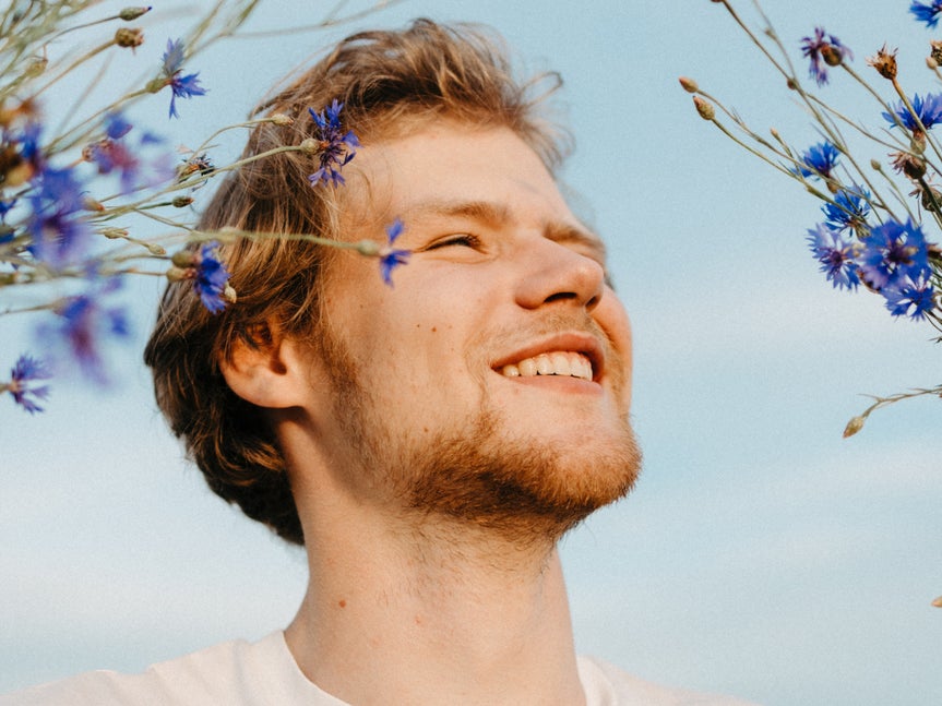 Foto de hombre sonriendo con el cielo azul de fondo y con flores en primer plano