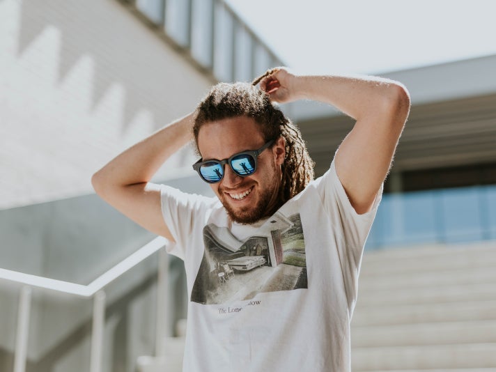 Foto de hombre atusándose el pelo y sonriendo con gafas de sol