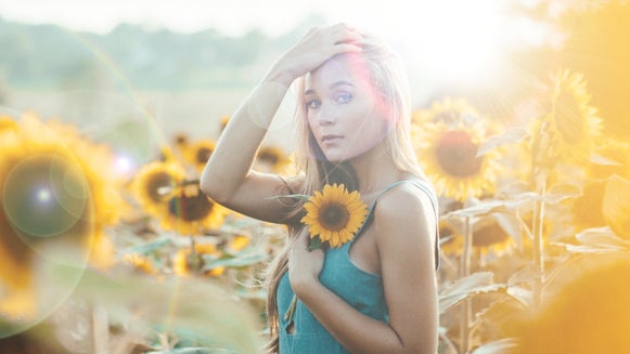 Woman in a sunflower field with bright lens flare creating a dreamy atmosphere