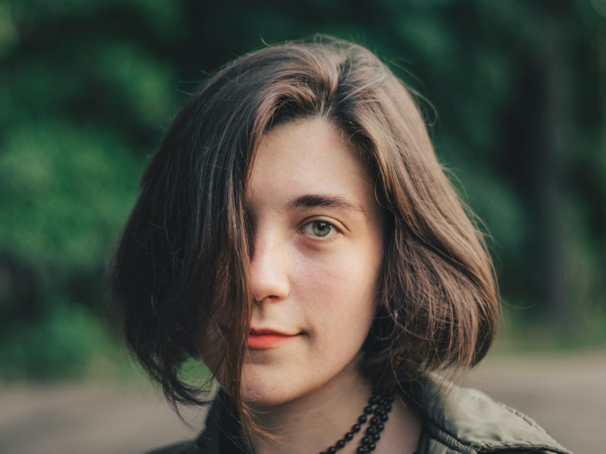 Brunette woman with chin-length hair and neutral expression in front of a blurred green background