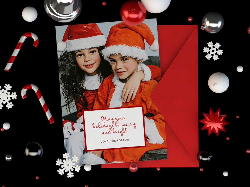 Printed holiday card featuring two kids in Santa outfits with festive decorations and red envelope